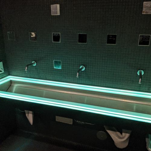 A wide trough sink lined with LEDs at Ground Kontrol. Small square mirrors line the wall above.