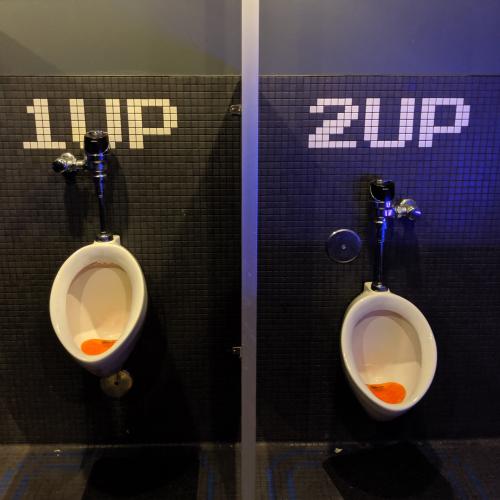 Two urinals with the text "1UP" and "2UP" above them in tile.